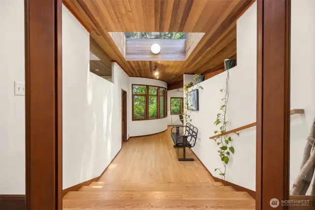 This artful main floor hallway is bathed in natural light from an oversized skylight and curved window wall, creating a bright, inviting path through the home
