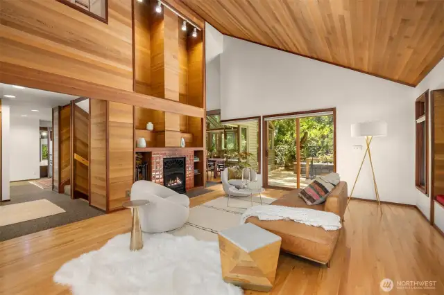 This stunning living room showcases soaring cedar-lined ceilings, a striking fireplace centerpiece, and seamless indoor-outdoor flow to a lush, private patio