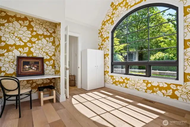 Charming flex space on the main floor bathed in natural light, featuring vaulted ceilings, a bold designer accent wall, and oversized arched window—ideal for a home office, creative studio, or cozy reading nook.