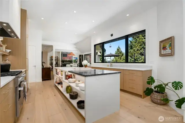 Designer kitchen with expansive center island, marble and soap stone countertops, open shelving, and sleek custom cabinetry. Oversized windows flood the space with natural light, offering picturesque views and a perfect blend of style and function.