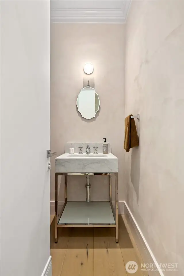 Chic powder room with a sculptural marble sink, elegant wall-mounted mirror, and soft plaster-finish walls—blending modern luxury with timeless style.