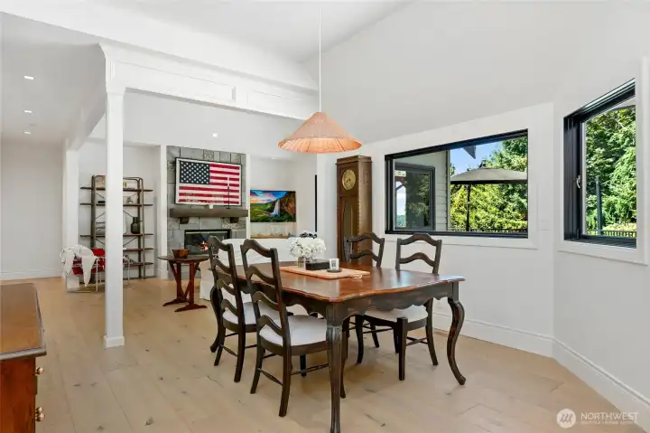 Bright dining area with large picture windows, vaulted ceilings, and wide-plank hardwood floors—seamlessly connected to the living space with a cozy fireplace and custom millwork detailing.
