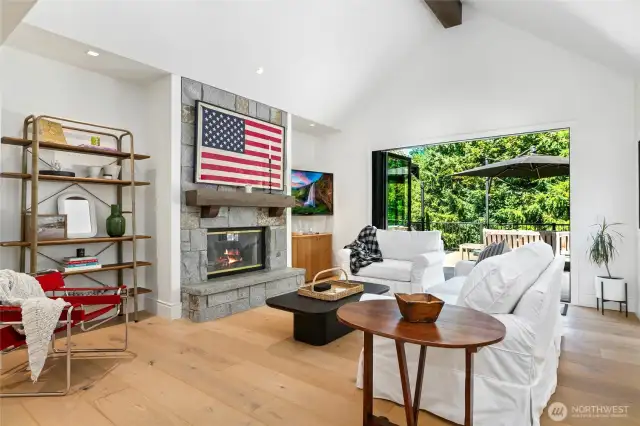 Inviting living room with vaulted ceilings, gas fireplace framed in stone, and seamless indoor-outdoor flow through a 10 foot  bi-folding sliding glass door to a private deck with views of Lake Sammamish.