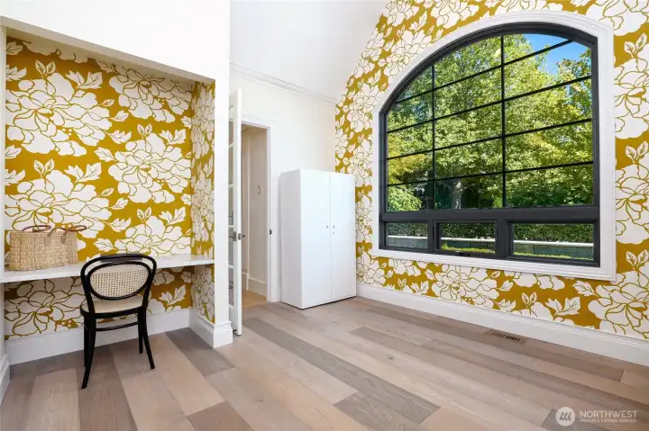 Charming flex space on the main floor bathed in natural light, featuring vaulted ceilings, a bold designer accent wall, and oversized arched window—ideal for a home office, creative studio, or cozy reading nook.