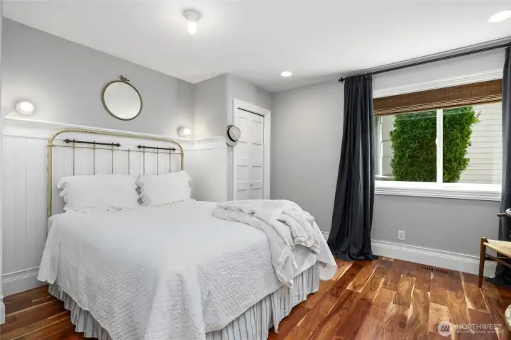 Charming first guest bedroom on the lower level featuring warm hardwood floors, classic wainscoting, and ample natural light—ideal for visitors or flexible living space.