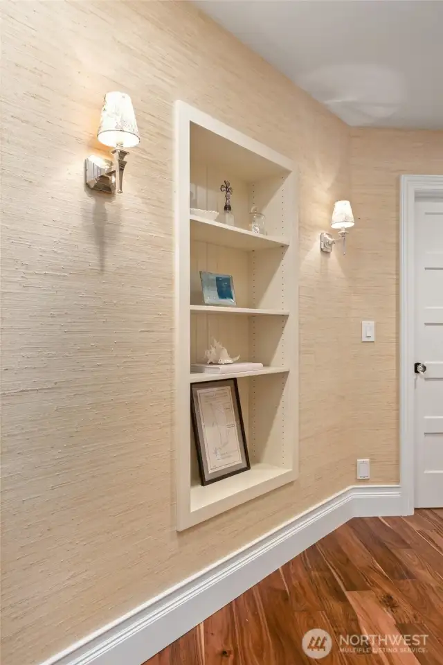 Charming hallway nook with built-in display shelving, grass cloth wall covering, and elegant sconces—adds character and functionality to the transitional space.