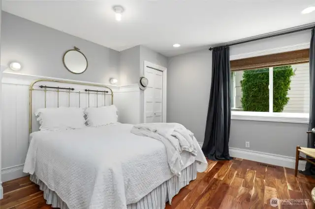 Charming first guest bedroom on the lower level featuring warm hardwood floors, classic wainscoting, and ample natural light—ideal for visitors or flexible living space.