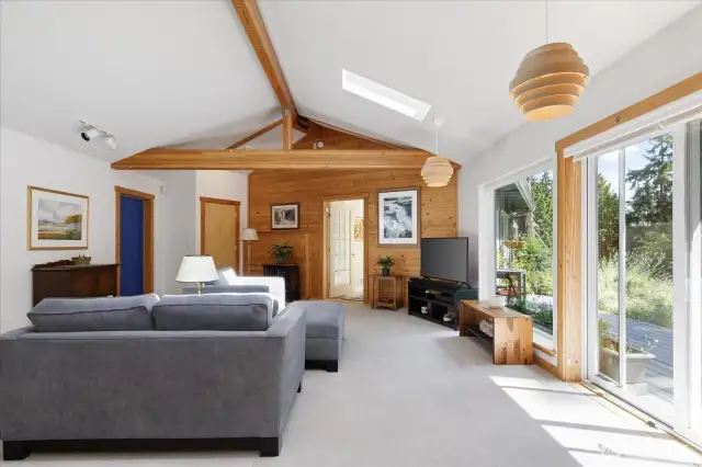 Bright living room with huge windows and a slider, plus a skylight too.  The wood hanging lamps remain.  The blue door to the left is the 'front door', and goes to the equipment room as well.