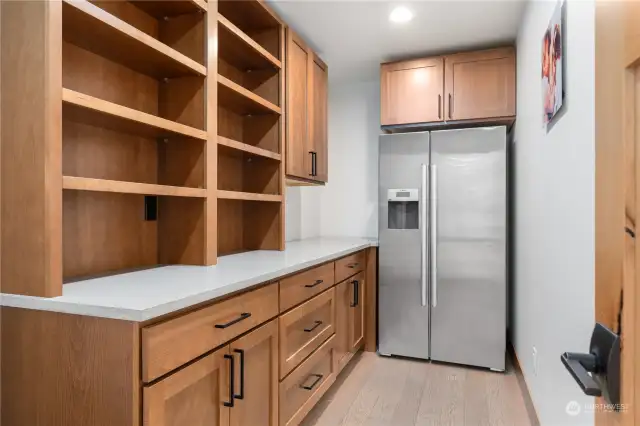 Main level walk-in pantry w/ quartz countertops, custom cabinetry and refrigerator.