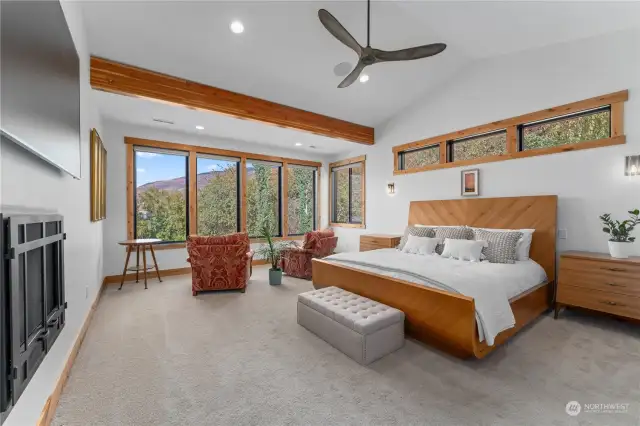 Main Level Primary Bedroom w/ fireplace, ceiling fan, seating area and large view windows.