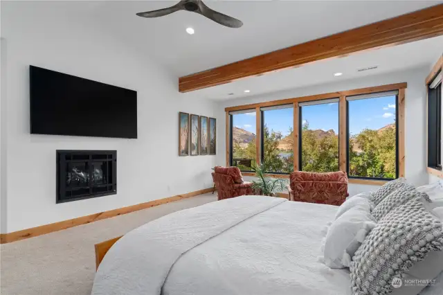 Main Level Primary Bedroom w/ fireplace, ceiling fan, seating area and large view windows.