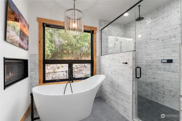 Main level Primary Bedroom Bathroom w/ radiant heated ceramic tile floors, a stand alone tub, electric fireplace and custom tile shower w/ Moen FGF faucet sensor system.