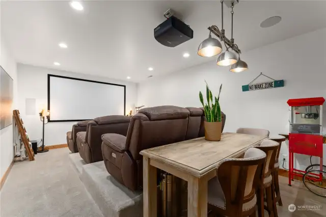 Lower level media room w/ theater seating, surround sound, 120” 4k projector screen plus a kitchenette/bar area w/ 3 keg kegerator and taps, freezer drawers, sink, beverage fridge, wood countertops and tile backsplash.