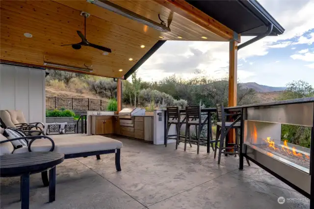 View of Main Level wraparound deck w/ dining and lounge area and outdoor kitchen w/ Memphis Grills Elite Stainless Steel Built-In Pellet Grill, built in cabinets, sink and refrigerator, leather-finish granite countertops, infrared overhead patio heaters and glass see-through fireplace.