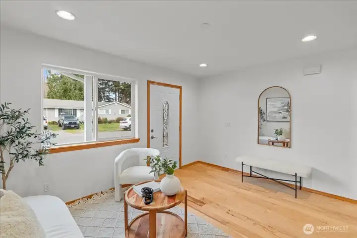 Bright entry living space with laminate flooring and recessed lighting. Open layout offers clear sightlines toward the hallway and staircase.