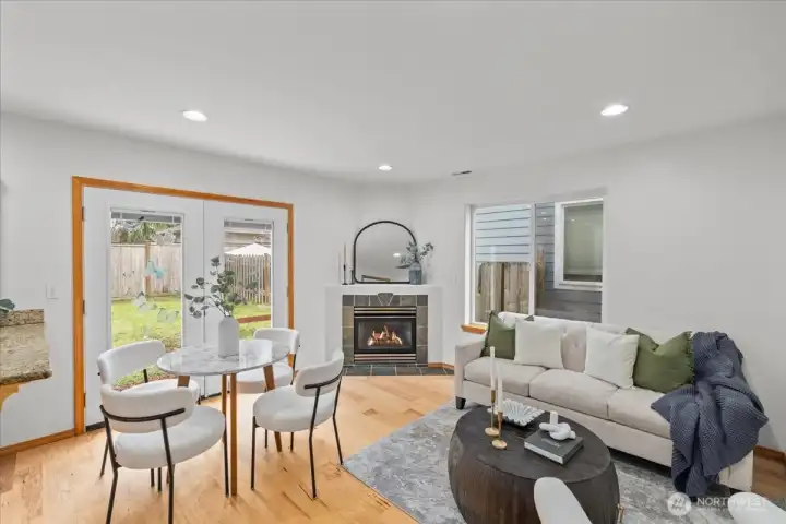 Open dining area with space for a table near glass doors leading to the backyard. Adjacent living area features a fireplace and large window for natural light.