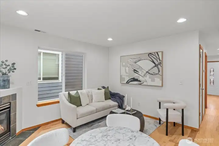 Living room with fireplace, recessed lighting, and a large window allowing natural light. Open layout connects the living area to the dining space and kitchen.