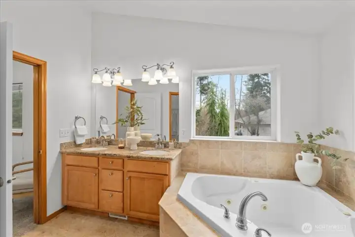 Spacious primary bathroom with dual-sink vanity, granite counters, soaking tub, and tiled flooring. Large window provides natural light and outdoor views.