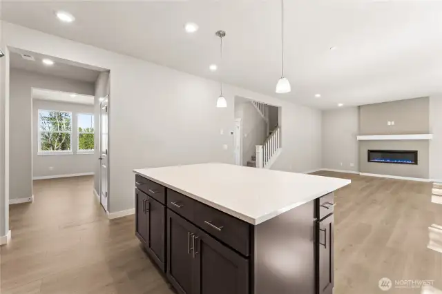 Large island, and open concept great room with fireplace. Photo is representational. Home is under construction and finishes, features, and colors may vary. See site agent for details.