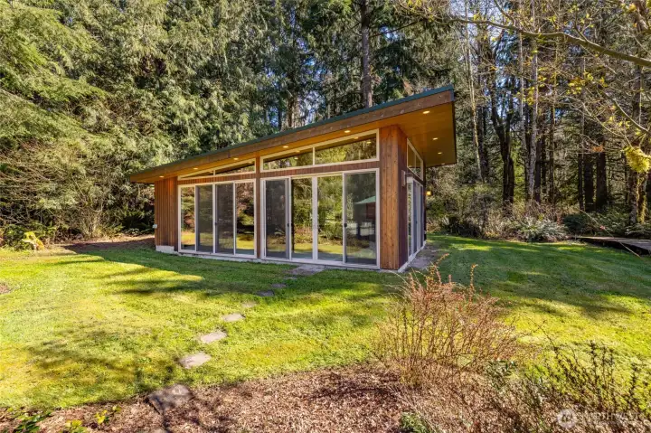 This charming 30x20 pool house has sliders lining two sides, soffit lighting, ceiling fan, and shower.  The above ground swim spa features a hot tub at one end.