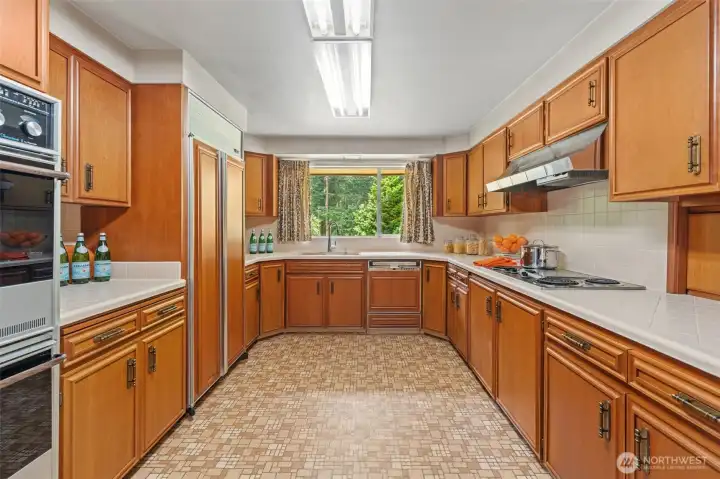 This spacious kitchen offers abundant cabinet and counter space, creating an efficient layout for everyday cooking and entertaining. The large picture window above the sink frames peaceful views, bringing the beauty of the outdoors into the heart of the home.