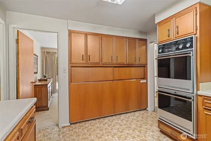 Storage is plentiful with an entire wall of built-in cabinetry, providing exceptional space for pantry items, small appliances, and serving essentials. The double wall ovens and timeless wood cabinetry create a kitchen ready for gatherings. The second pass-through keeps the dining room connected for easy serving and conversation OR, when shut as seen here, provides privacy from the kitchen.