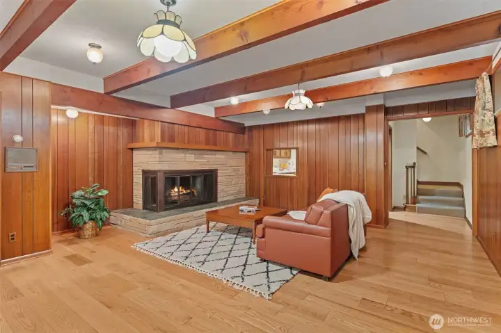 The lower level family room is so stylish with exposed wood beams and rich wood-paneled walls. It creates timeless architectural character throughout the space. A stone wrapped fireplace serves as the centerpiece, making this an inviting place to gather, relax, and entertain.