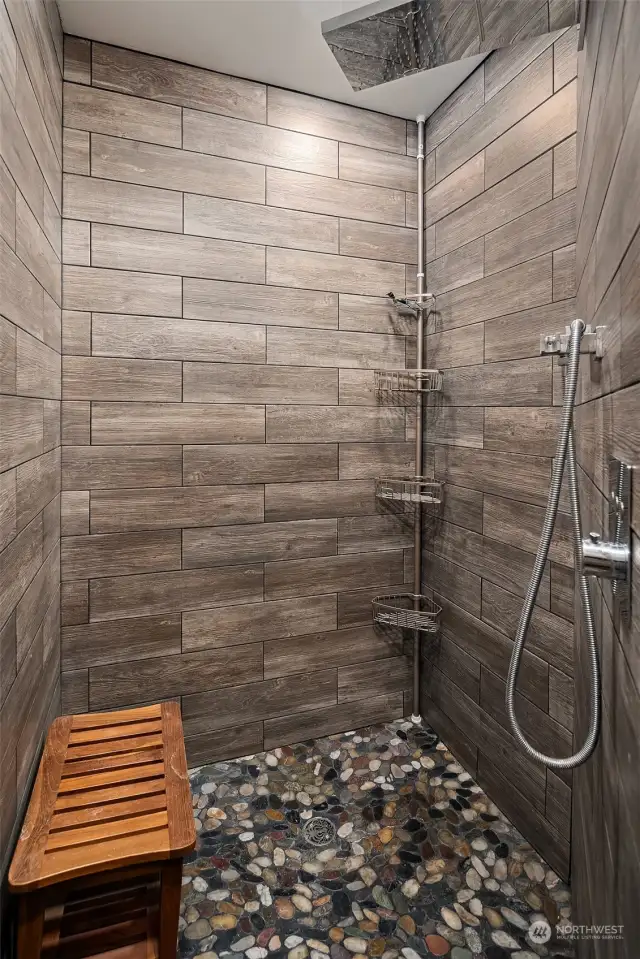 Shower room with large walk-in shower with slate tile, rock flooring, waterfall/stream shower head, and towel warmer.