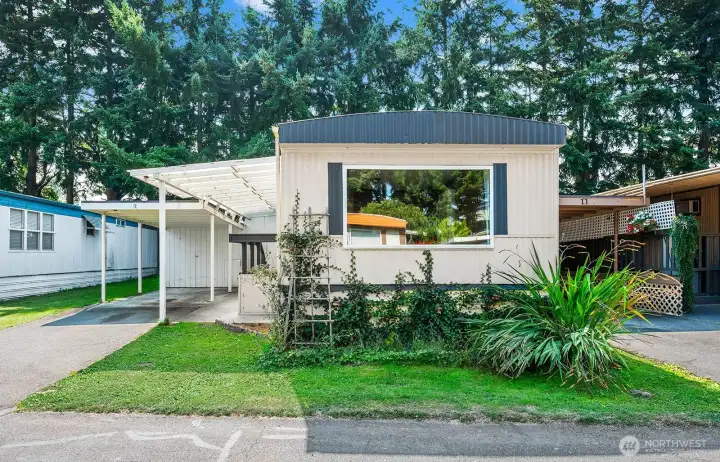 Front view of the home with large picture window, covered carport, and low-maintenance yard.