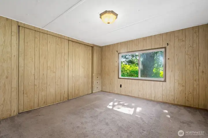 Bedroom with a wide closet and built-in drawers, filled with natural light from the large window.