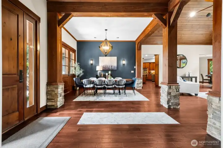 Framed by substantial timber posts with stone bases, the formal dining space makes a striking impression—anchored by a statement light fixture and rich accent wall, with clean sightlines that enhance the home’s open yet defined design.