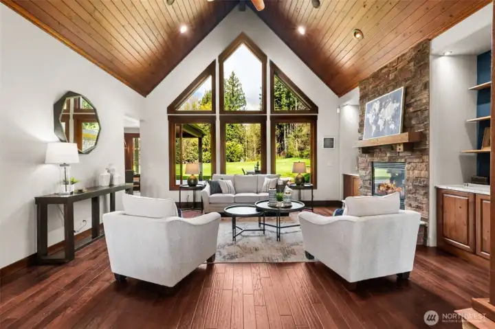 A stunning great room takes center stage with a soaring vaulted tongue-and-groove ceiling and dramatic wall of windows that frame peaceful, park-like views. Anchored by a floor-to-ceiling stone fireplace, the space blends natural warmth with refined Northwest style.