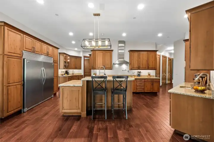 Designed with the cook in mind, the spacious kitchen offers extensive cabinetry, sprawling countertops, and a substantial center island with bar seating. Stainless steel appliances, a professional-style range hood, and thoughtful layout make it ideal for everyday living and entertaining alike.