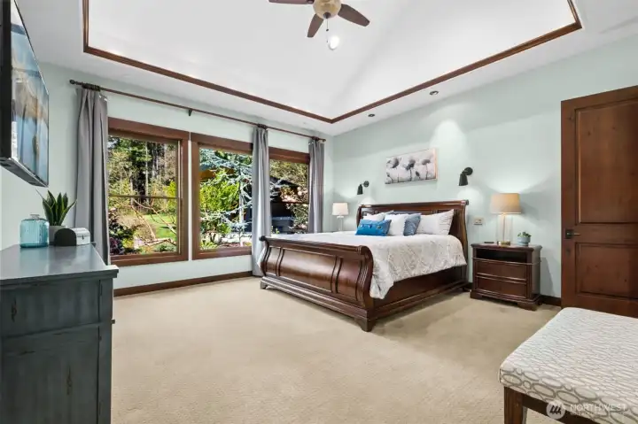 Thoughtfully positioned for privacy, the primary suite is a true retreat—set just beyond the main living spaces. A refined tray ceiling with crown molding detail enhances the room’s sense of space and adds a touch of classic architectural character. Filled with natural light and calming garden views