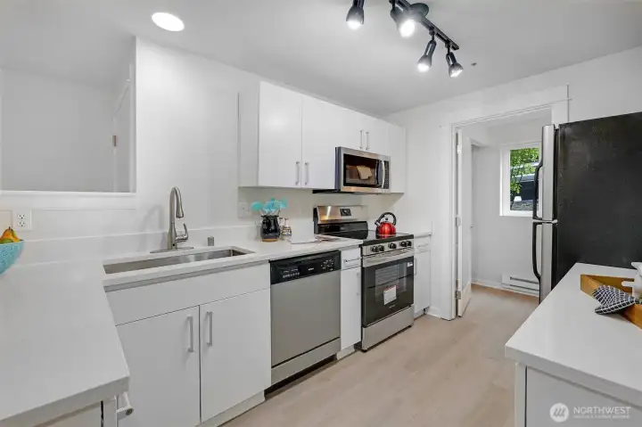A closer look at the kitchen reveals a deep under-mount sink with modern pull-down faucet, electric range with microwave hood, and full-size dishwasher—all framed by crisp solid-surface counters that make cleanup a breeze.