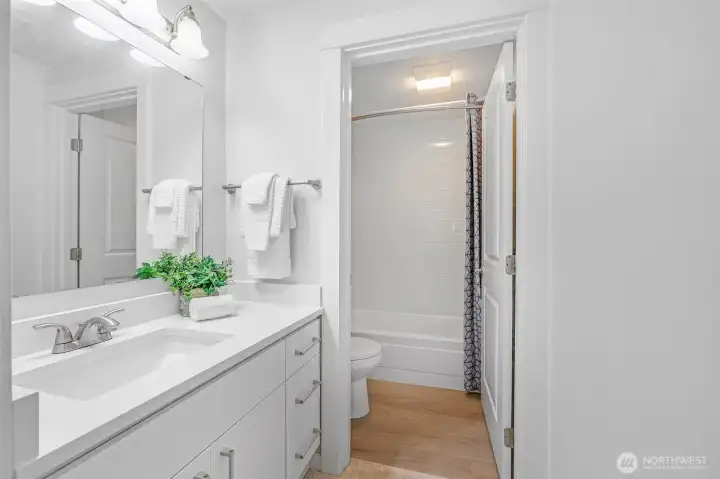 The ensuite bath showcases a sleek quartz-slab vanity, brushed-nickel fixtures, and a tub/shower combo wrapped in timeless subway tile—an easy-care space with fresh, contemporary appeal.