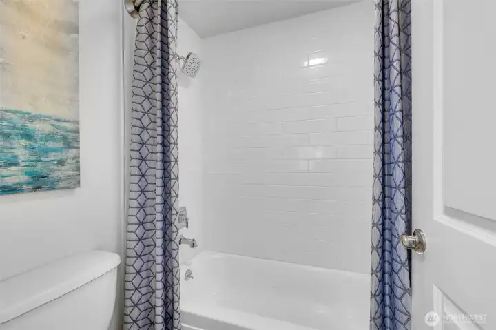Close-up of the tub/shower reveals full-height white tile and an adjustable rain-style showerhead, delivering spa-like simplicity and durability for everyday use.