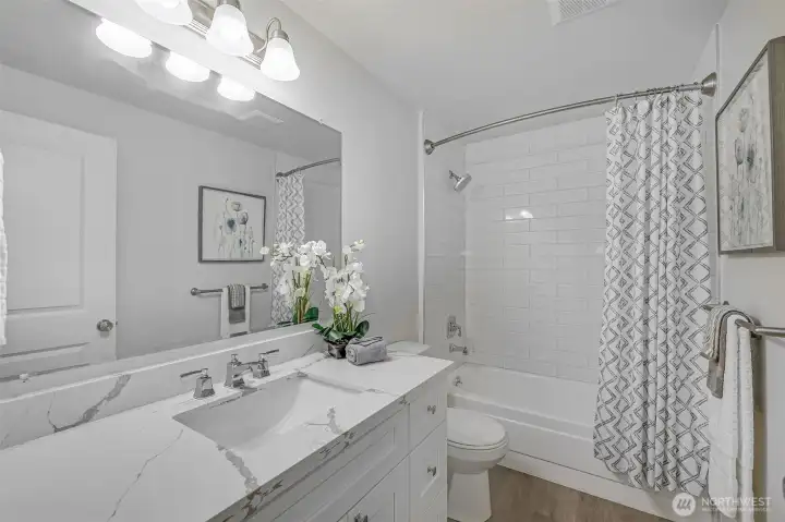 The main bath is fully updated with a double-sink quartz vanity, generous storage drawers, and a subway-tiled tub/shower—ideal for shared living or accommodating visitors.