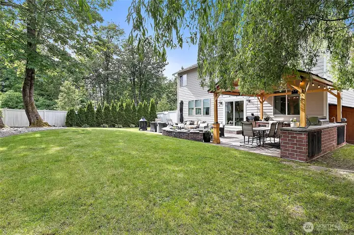 Private backyard retreat features mature landscaping, expansive patio including gas fire pit area, and a covered outdoor kitchenette.