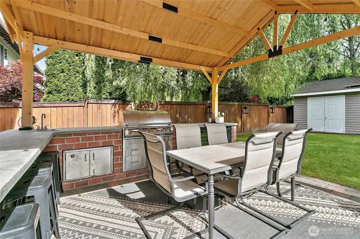 Covered outdoor kitchenette features bar seating, a built-in BBQ, pizza oven, mini fridge, and wine refrigerator-perfect for year round entertaining!