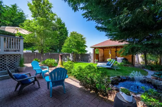 The backyard oasis is a standout, complete with a lush lawn, covered gazebo, water feature, and lounging space—ideal for entertaining or simply enjoying a summer day.