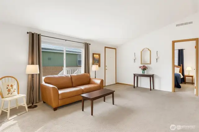 Virtually staged living room with a leather couch, coffee table, and primary bedroom with curtains and queen sized bed in it.