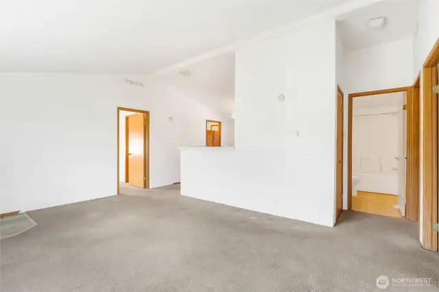 From a corner in the living room, you can see the primary bedroom door to the left, the kitchen half-counter, and the doorways to the other two bedrooms and full main bathroom.