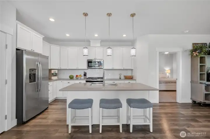 Kitchen is well designed with plenty of cabinet and counter space.  Great entertaining island. Door on right leads to primary bedroom and ensuite.