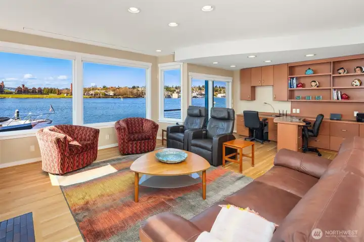 The spacious great room: seating and fireplace by the windows, a built-in two-person office tucked into the corner with full views of all waterfront activities from every angle.