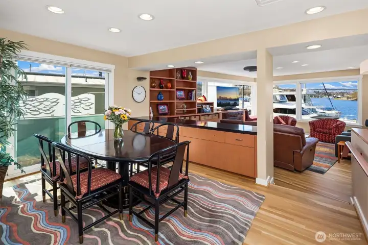 From the dining table, the view runs uninterrupted past the credenza and living room to Lake Union — boats in the foreground, water and sky everywhere.