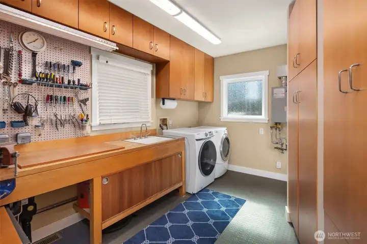 The downstairs utility room is more workshop than laundry room, with a butcher-block workbench, deep sink, pegboard wall, full laundry, and a tankless water heater tucked behind a wall of cherry cabinetry.