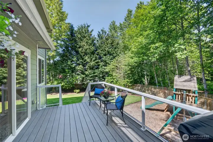 Deck off back of home looks over fenced back yard and play area.