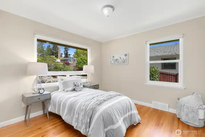 Bright second bedroom with dual windows and refinished hardwood floors overlooks front yard garden.