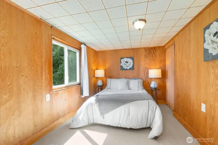 Cozy lower-level bedroom with classic wood paneling and a garden-view window.